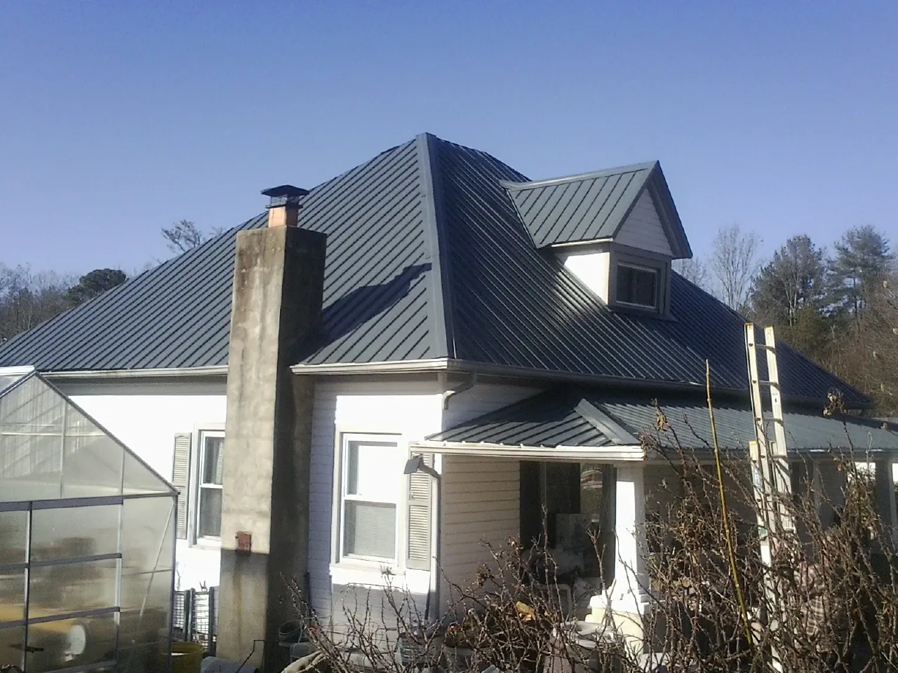 Dark blue standing seam metal roof on a white farmhouse with dormer — Slate & Tile Roof Repair by Roofing Brothers in Whitfield