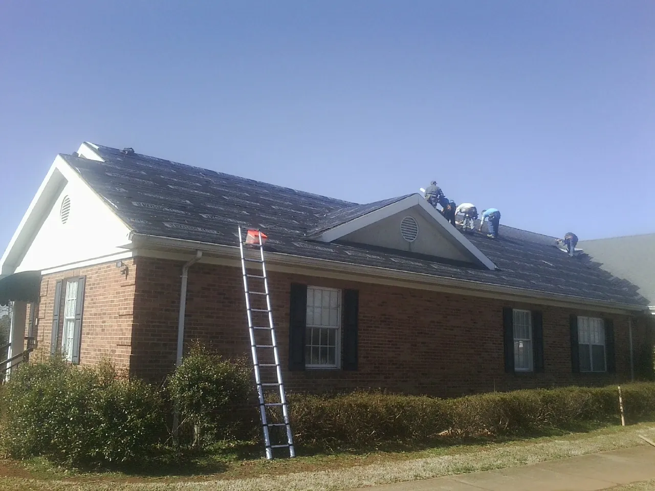 Crew tearing shingles off a brick ranch roof with a ladder set — Metal Roof Repair work by our crew in Whitfield