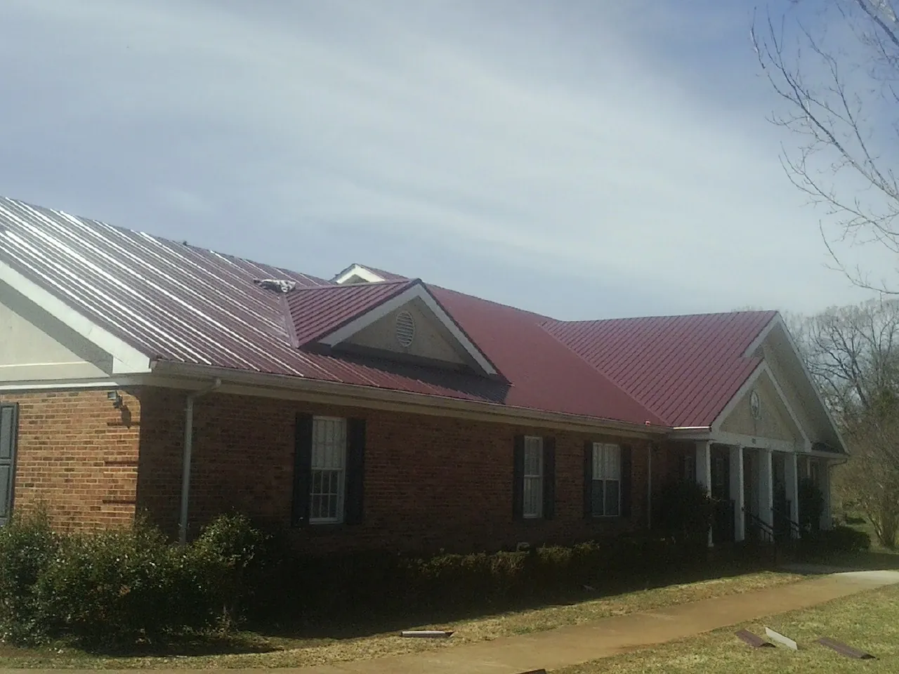 Red metal roof with gabled entries on a long brick building, from a Hail Damage Roof Repair job in Whitfield