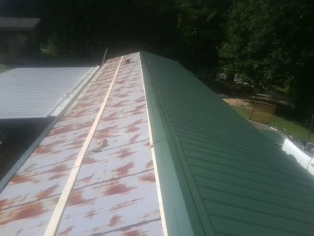 Old rusted panels beside newly installed green metal roofing — Wind Damage Roof Repair by Roofing Brothers in Whitfield