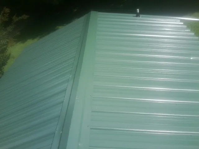 New green metal panels meeting at the ridge of a roof — Flat Roof Repair work by our crew in Whitfield