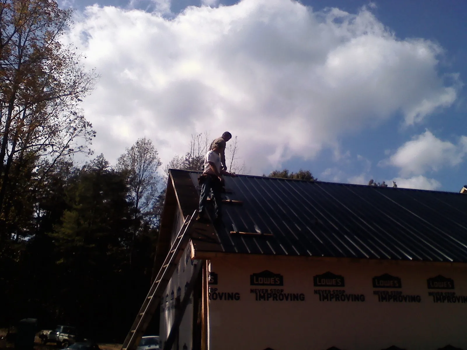Roofer fastening dark metal panels high against a cloudy sky, from a Roof Inspection job in Whitfield